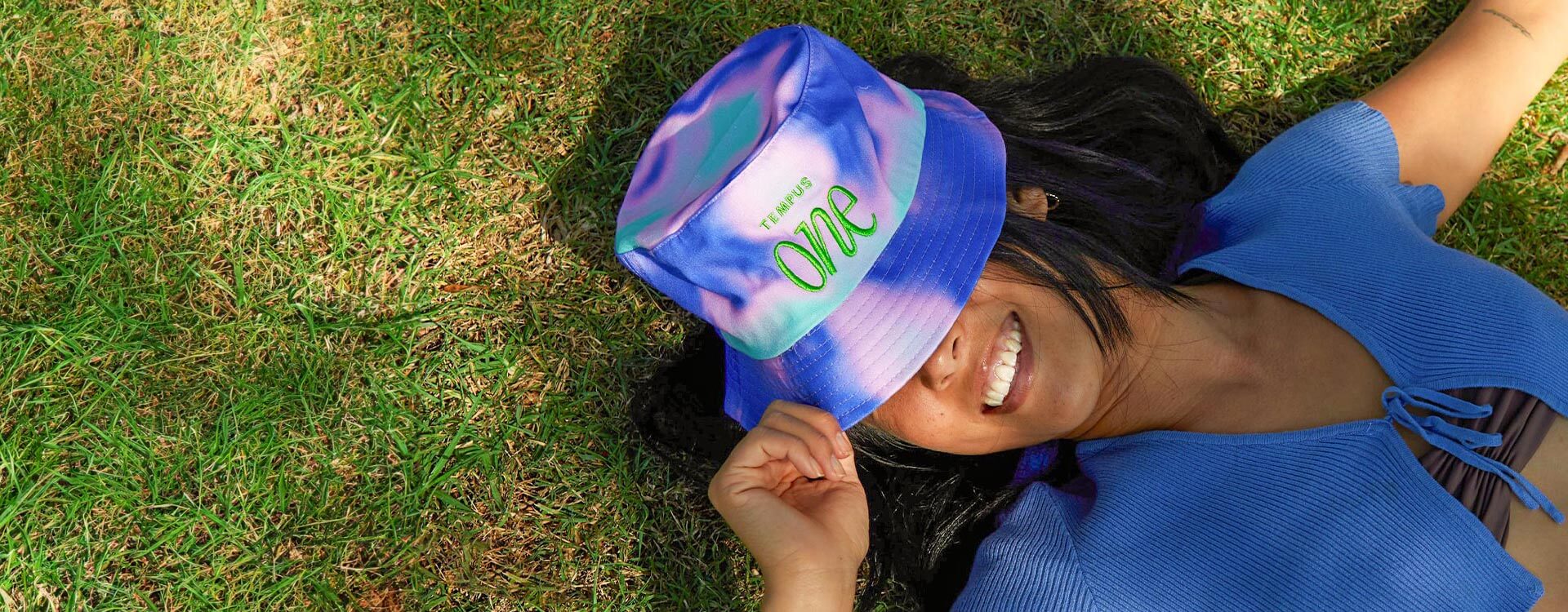 girl lying down in grass wearing a blue tie-dye Tempus One bucket hat